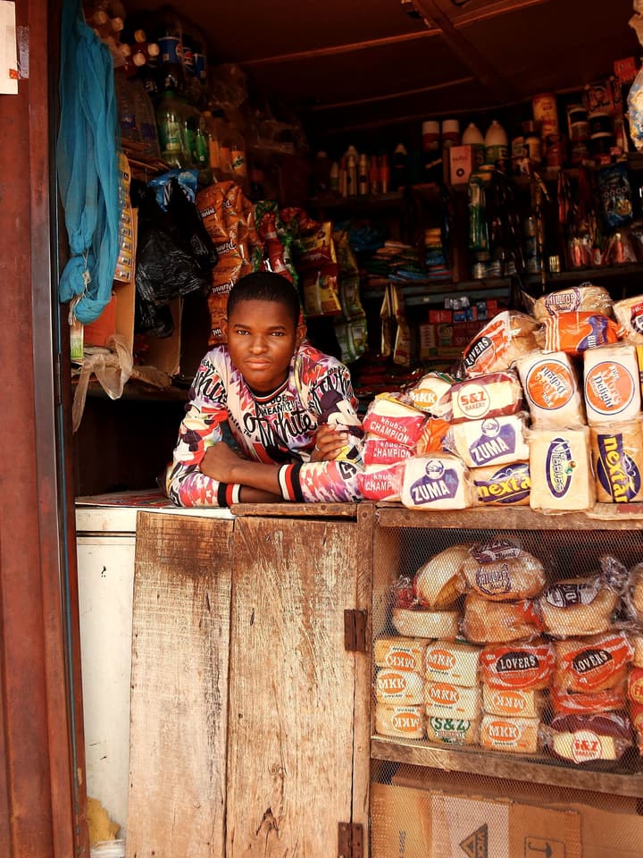 A young man leaning on the counter of a kiosk stacked with bread
