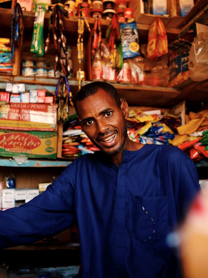 A smiling shopkeeper behind the counter of a well-stocked shop
